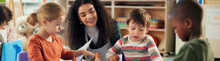 Female educator smiling as children colour and draw