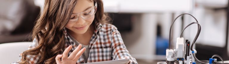 Female student typing on iPad with robot on table