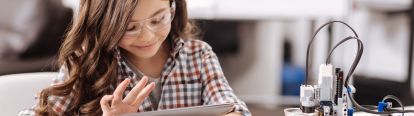 Female student typing on iPad with robot on table