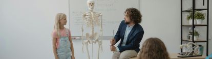 Male teacher showing skeleton to student in biology class