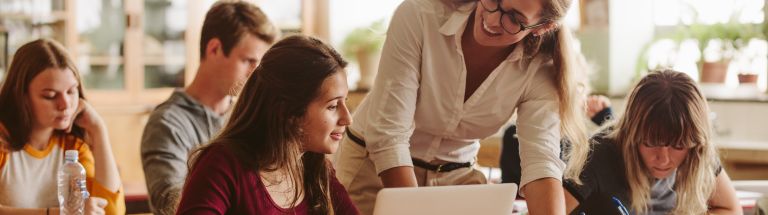 Teacher leaning over student's desk and looking at student.